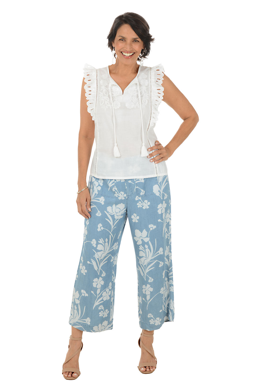 Woman wearing a white sleeveless top with lace details and blue floral pants on a white background