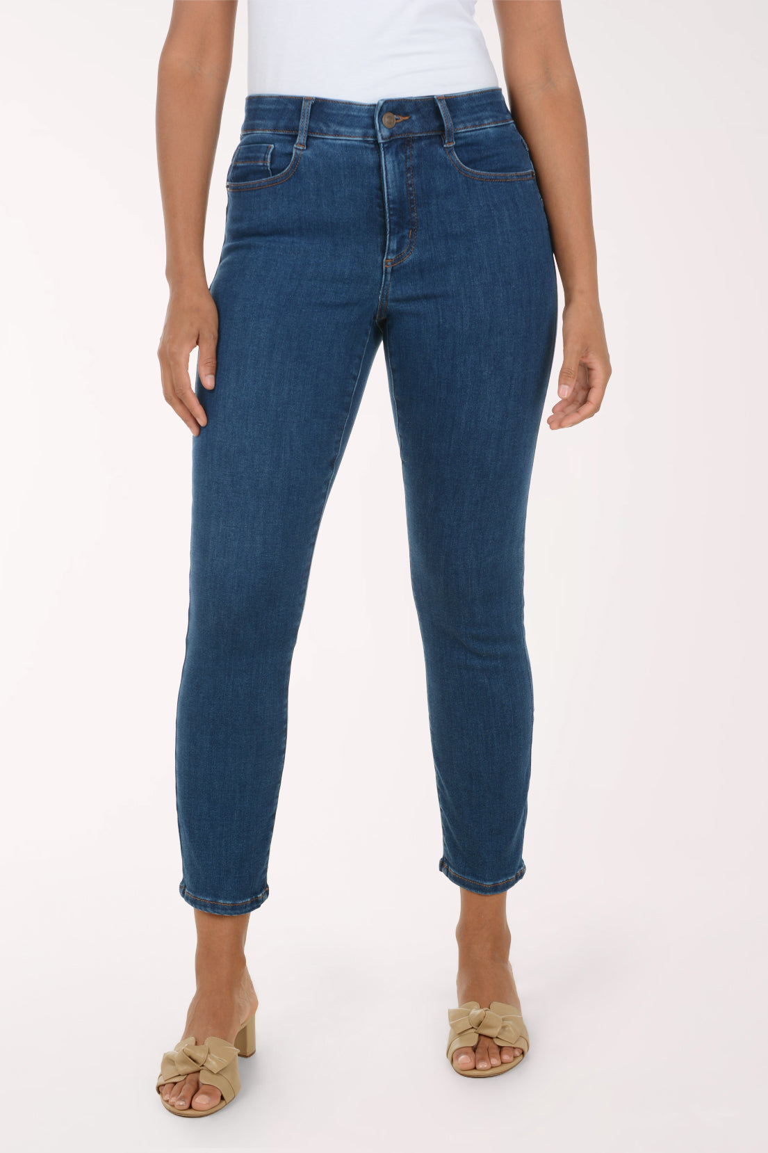 A model wearing a pair of dark blue skinny jeans with a white top and beige heeled sandals, shown from the waist down against a plain white studio background.