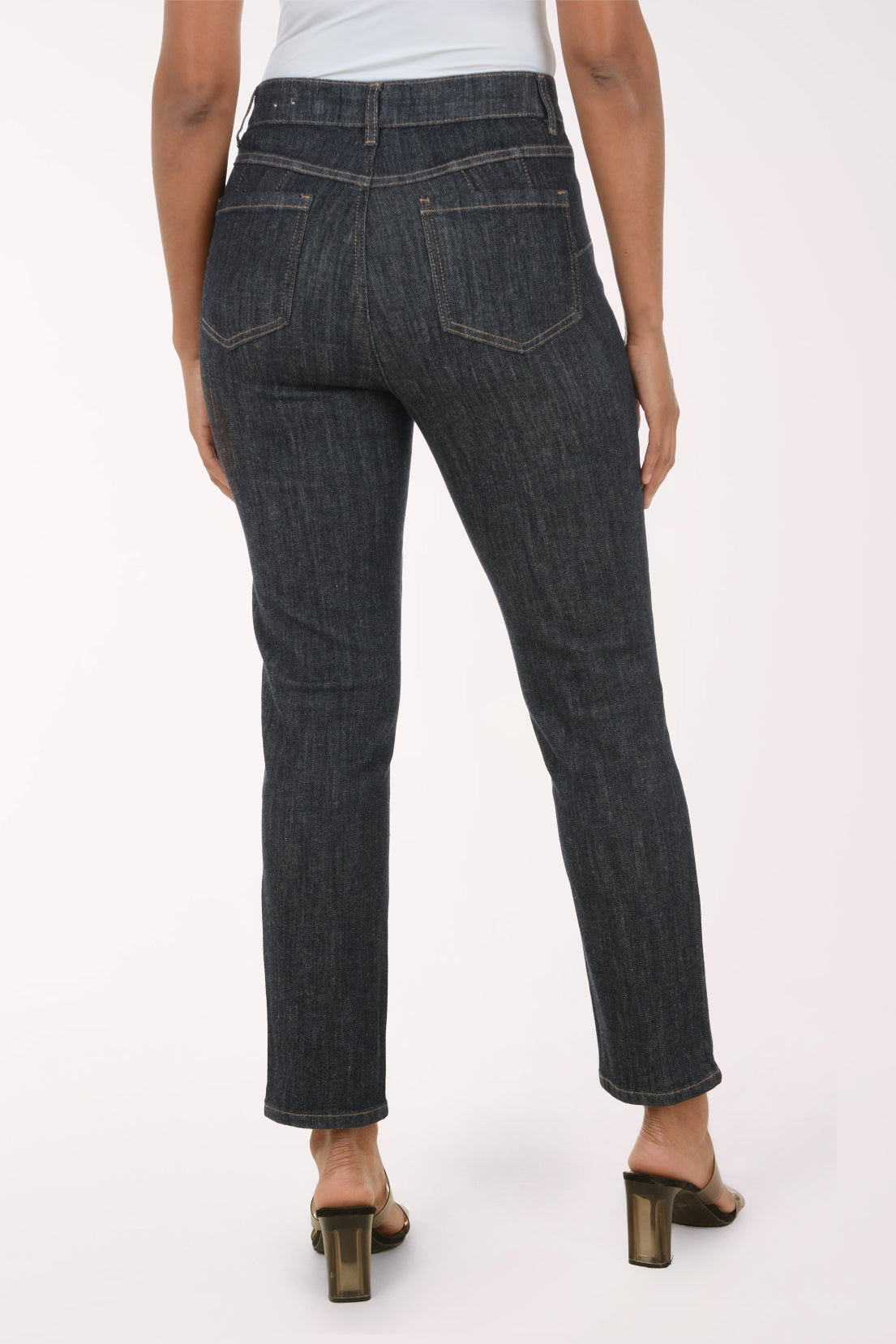 A model wearing dark gray slim-fit denim jeans with a light gray top and metallic brown heeled sandals, shown from the waist down against a plain white studio background.