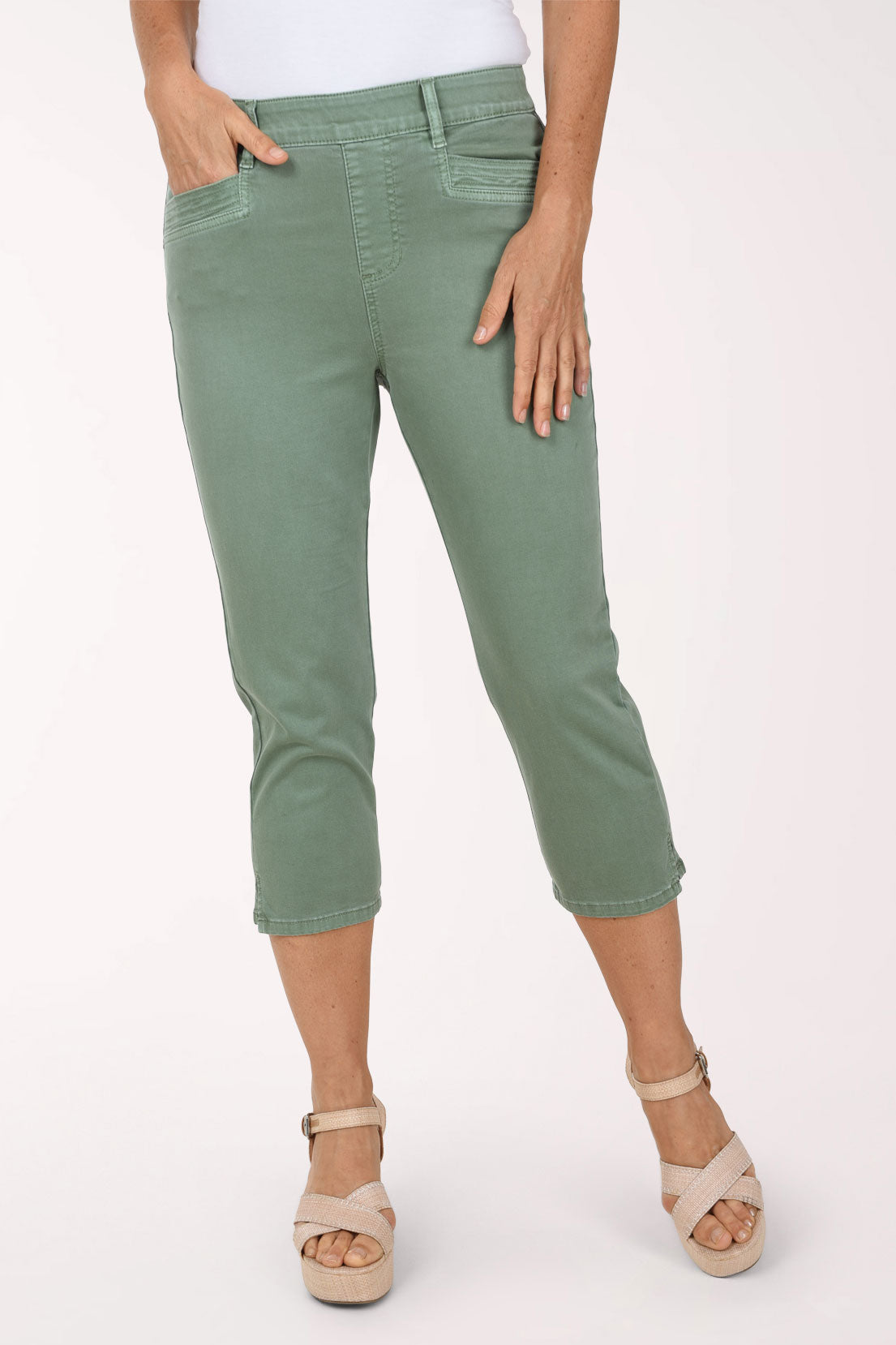Front view of sage green Moss stretch denim capri pants with a pull-on waistband, belt loops, topstitched front pockets and faux fly, worn with a white top and nude platform sandals.