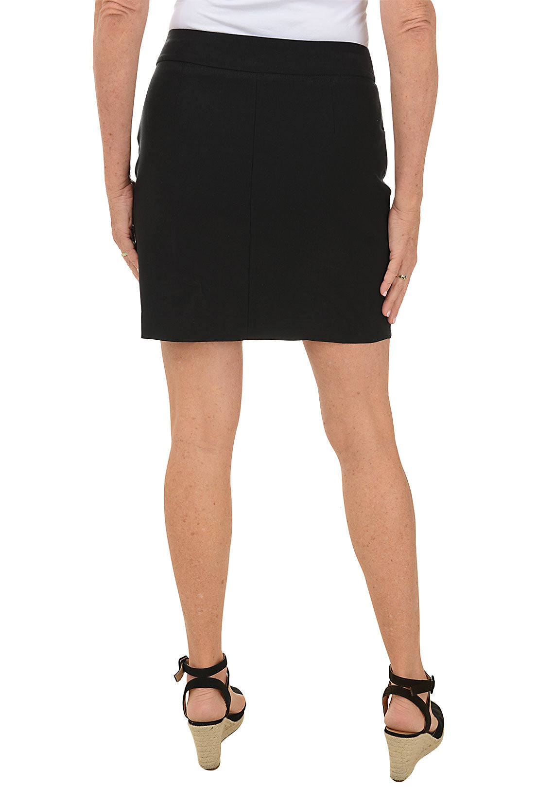 A woman wearing a black pull-on skort with a curved tulip hemline, paired with a white top. Back shot.