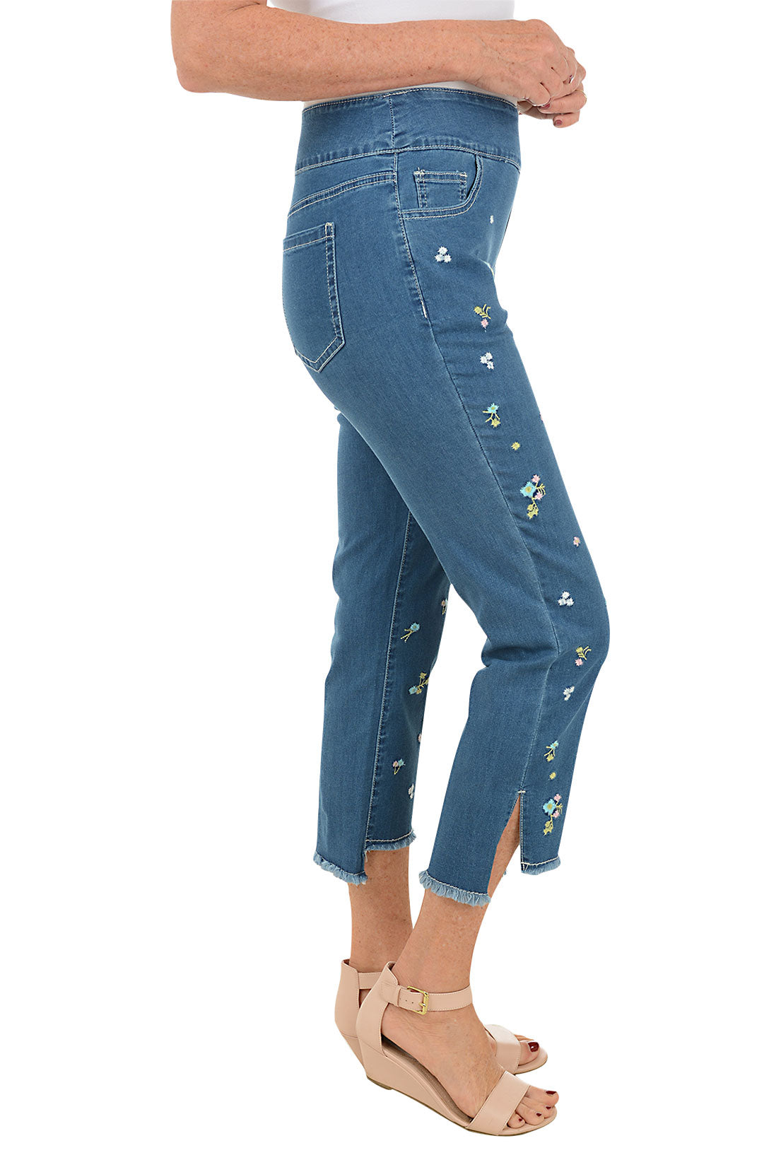 A pair of blue denim ankle pants with floral embroidery, a pull-on style with a 5-pocket design, and frayed hem with side slits. Side shot.
