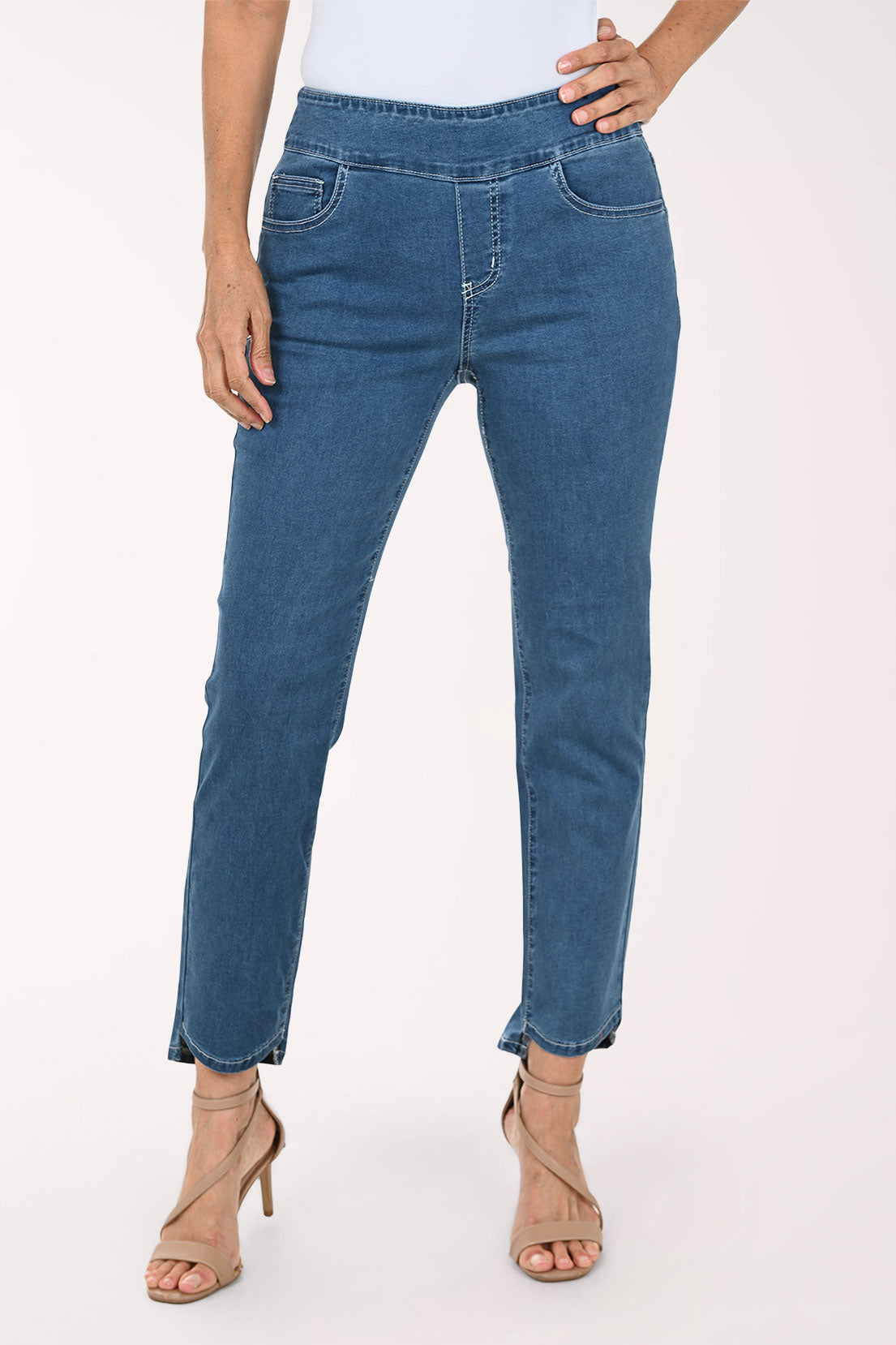 A model wearing medium wash blue denim jeans with a straight-to-regular leg fit, styled with beige high-heeled sandals against a plain white studio background.