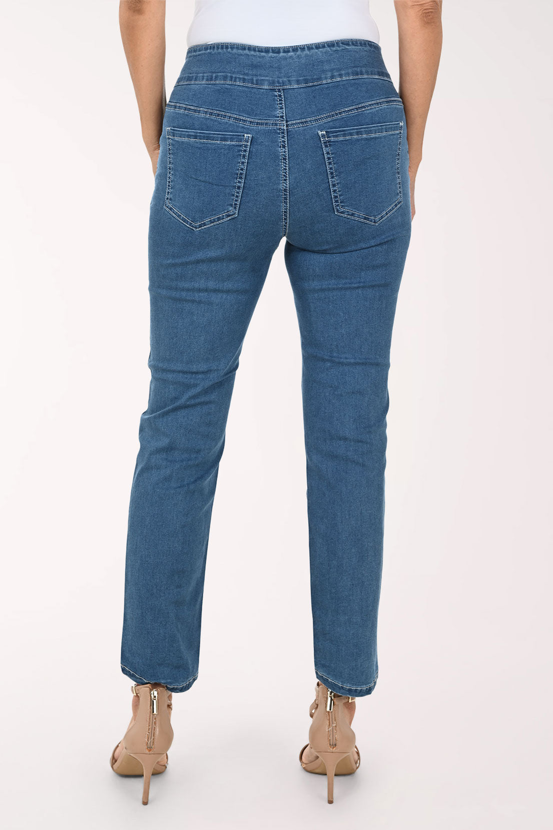 A model wearing medium wash blue denim jeans with a straight-to-regular leg fit, styled with beige high-heeled sandals against a plain white studio background.