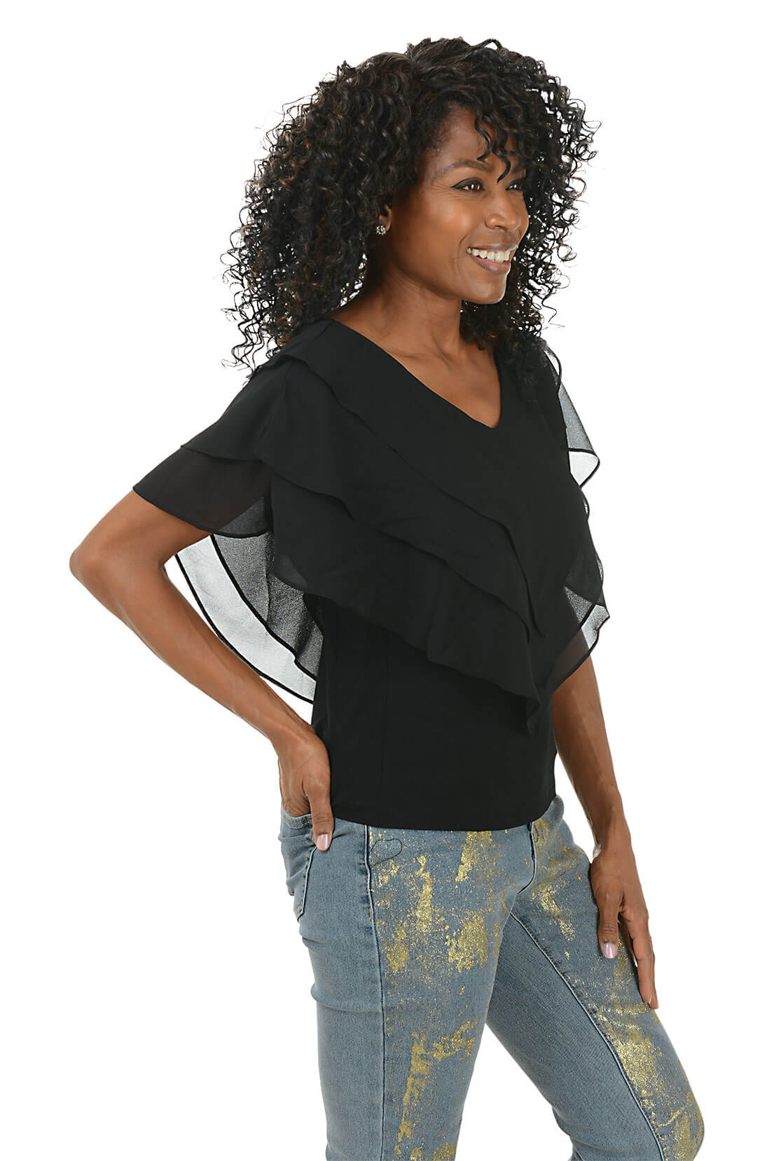 Woman wearing a black top with sheer sleeves and patterned pants on a white background. Side shot.