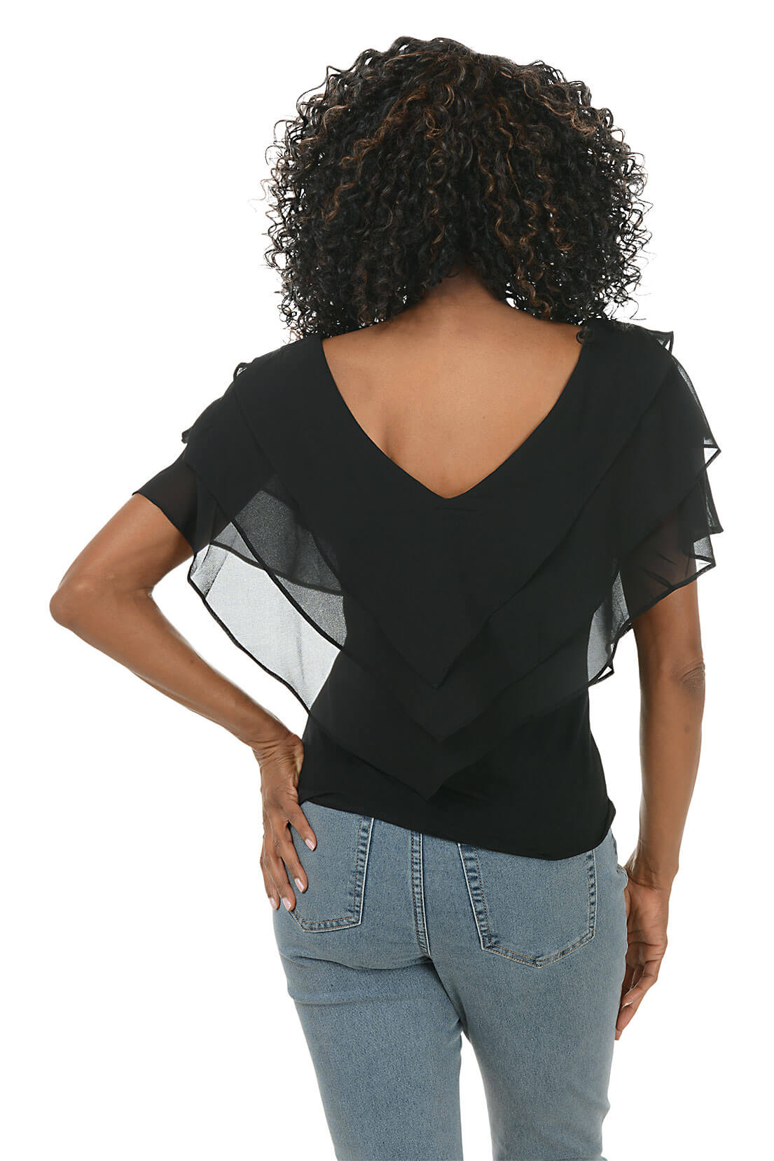 Woman wearing a black top with sheer sleeves and patterned pants on a white background. Back shot.