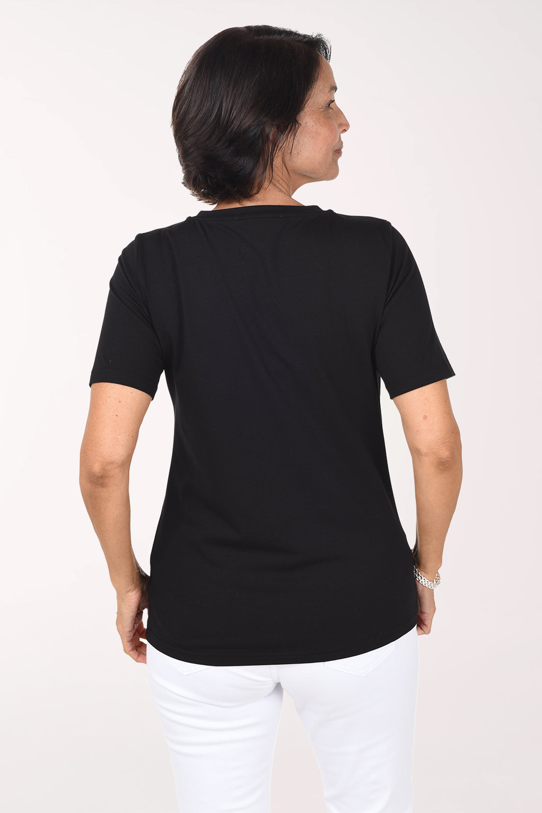 Back view of the black V-neck tee showing a plain black back and straight hem, worn with white pants.