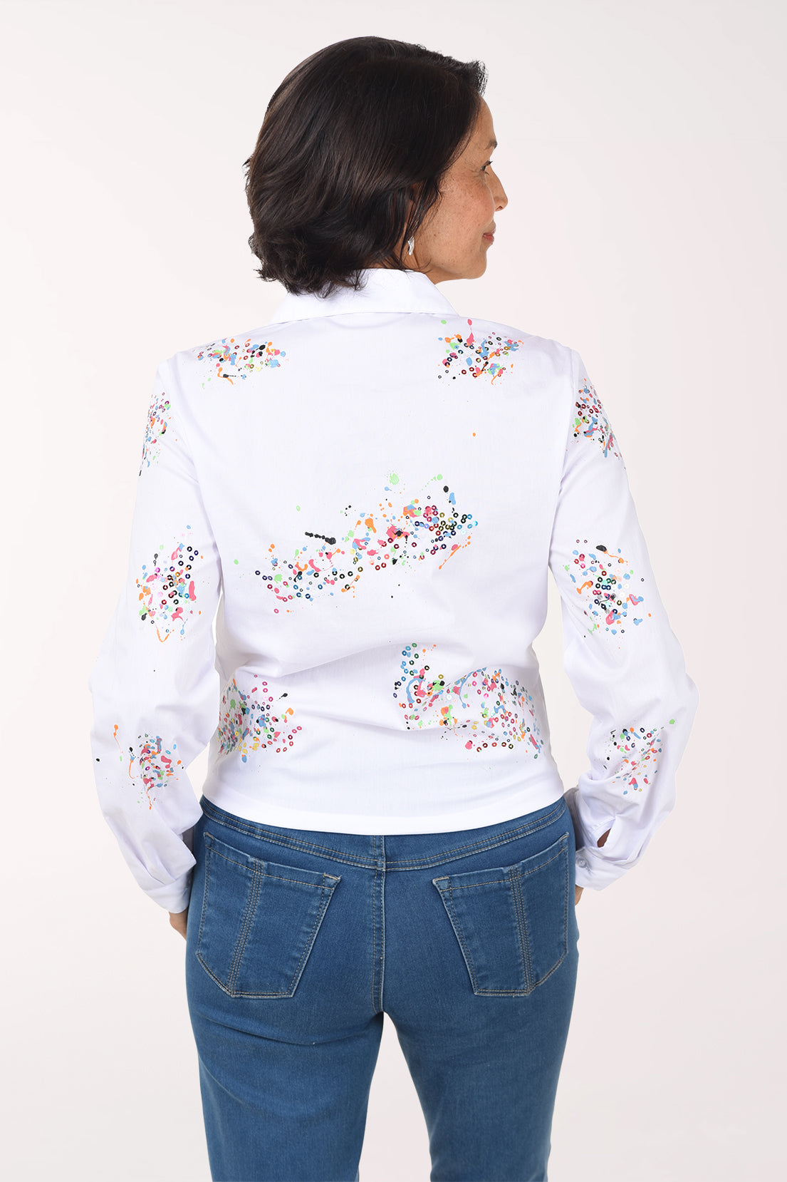 Back view of the white shirt showing paint speckle and sequin clusters across the back and sleeves, worn with jeans.