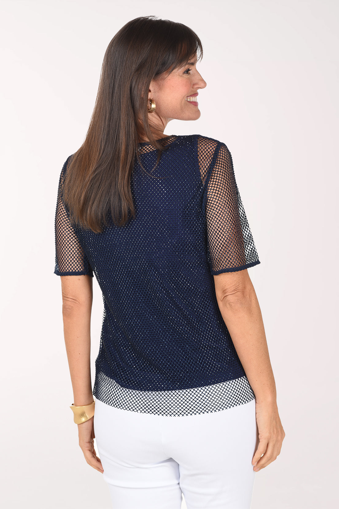Back view of the navy rhinestone mesh blouse showing the open mesh over the tank and the sheer short sleeves, worn with white pants.
