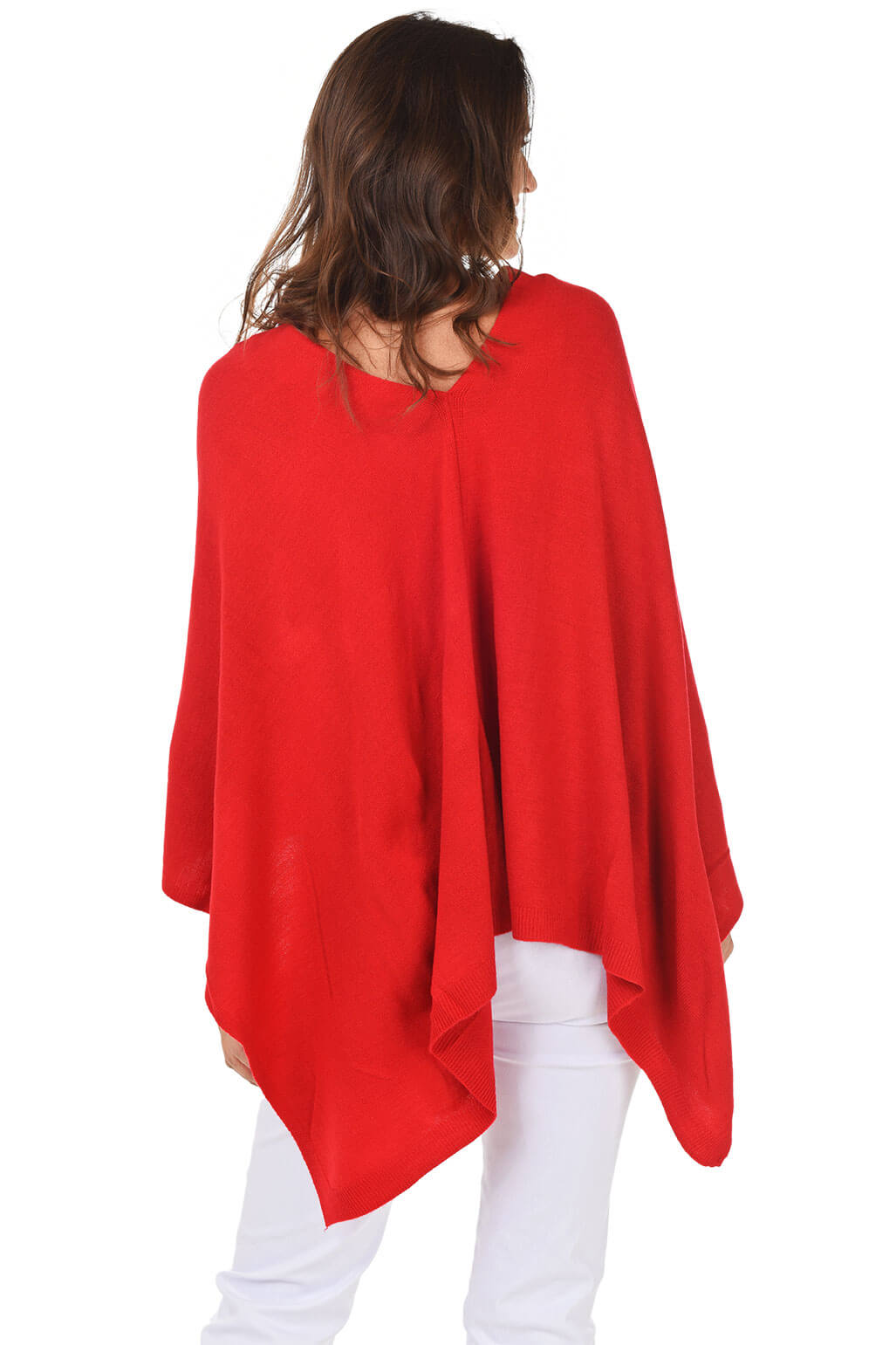 A woman wearing a red popover poncho with white pants. Back shot.