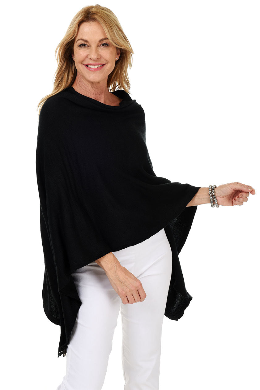 A woman wearing a black popover poncho with white pants.