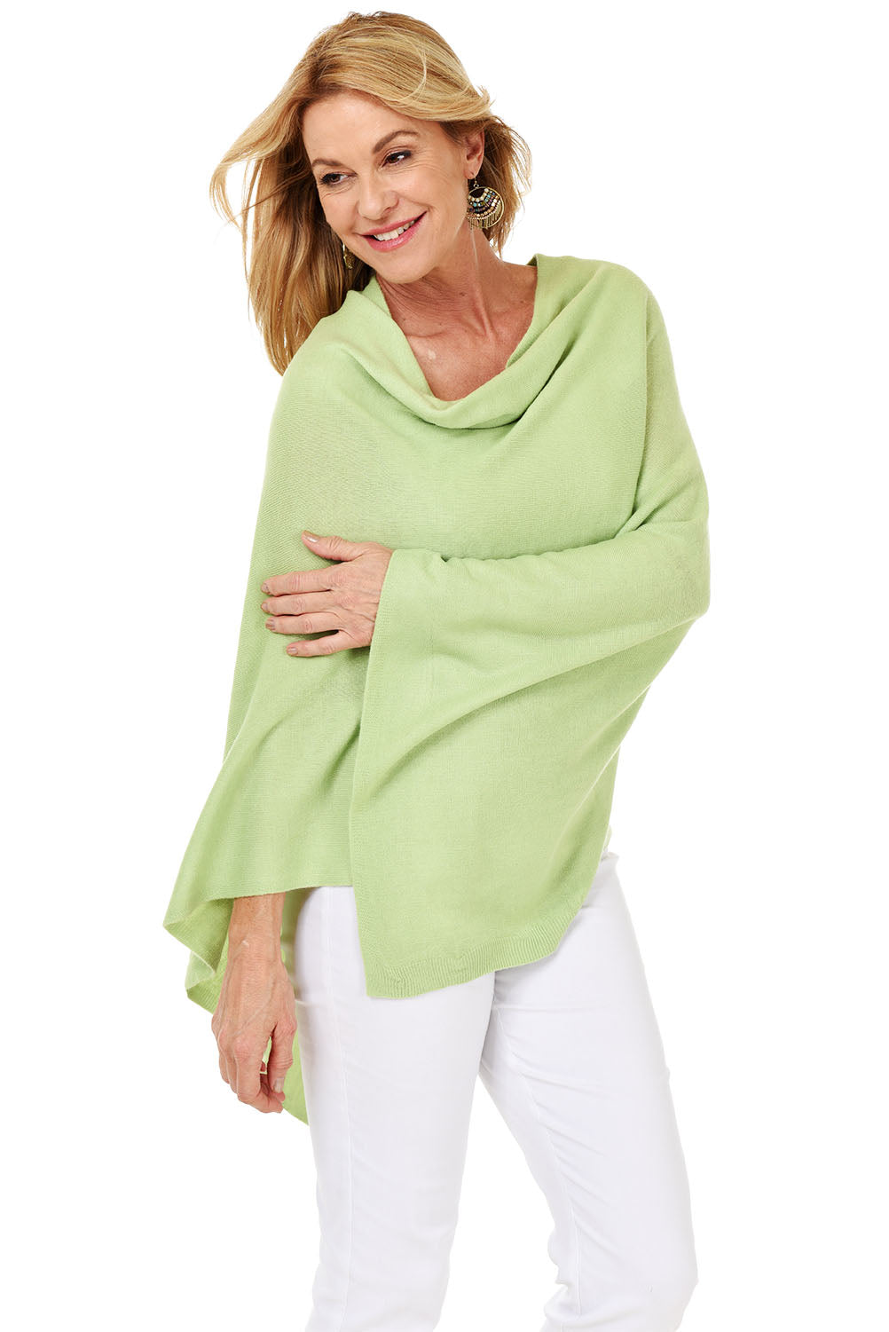 A woman wearing a green popover poncho with white pants.