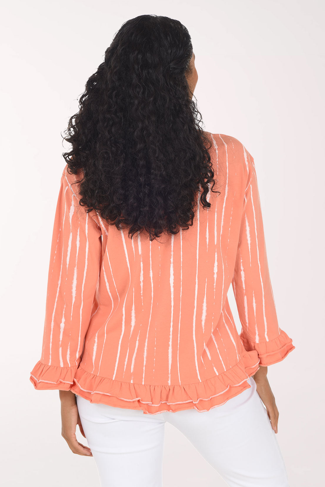 Woman wearing an orange and white 3/4 sleeve top with a tiered ruffled hem and cuffs