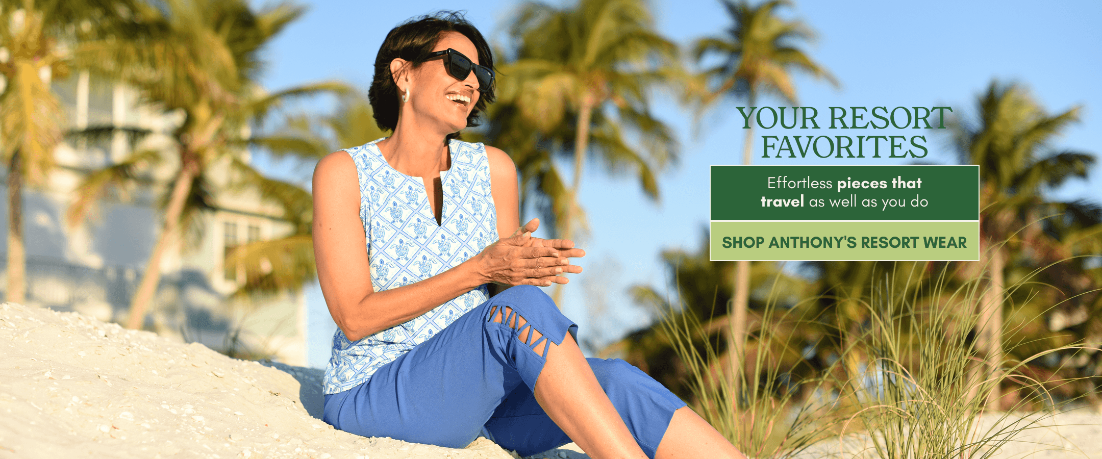 A woman wearing a sleeveless light blue and white patterned top and blue pants sits on a sandy beach with palm trees and resort buildings in the background. Text on the right reads 'YOUR RESORT FAVORITES' and 'SHOP ANTHONY'S RESORT WEAR.