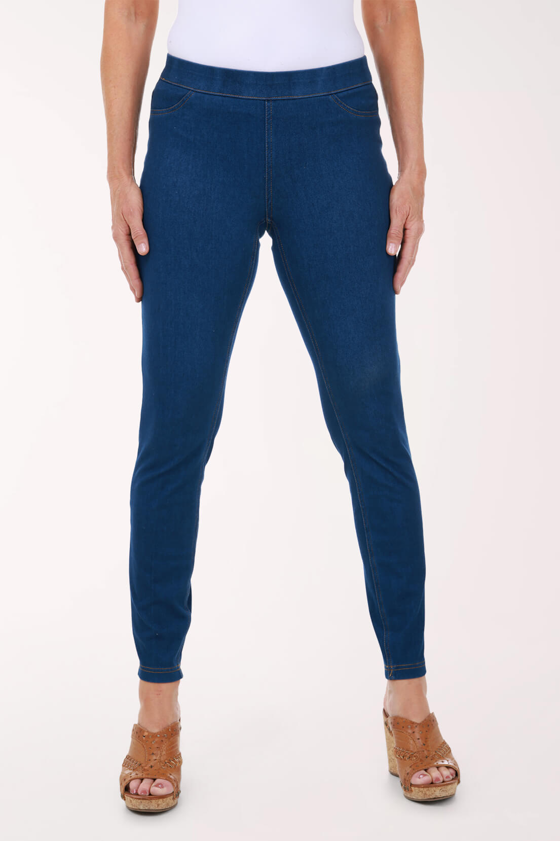 A front view of medium wash skinny pull-on jeggings with a smooth elastic waistband, worn with tan wedge sandals.