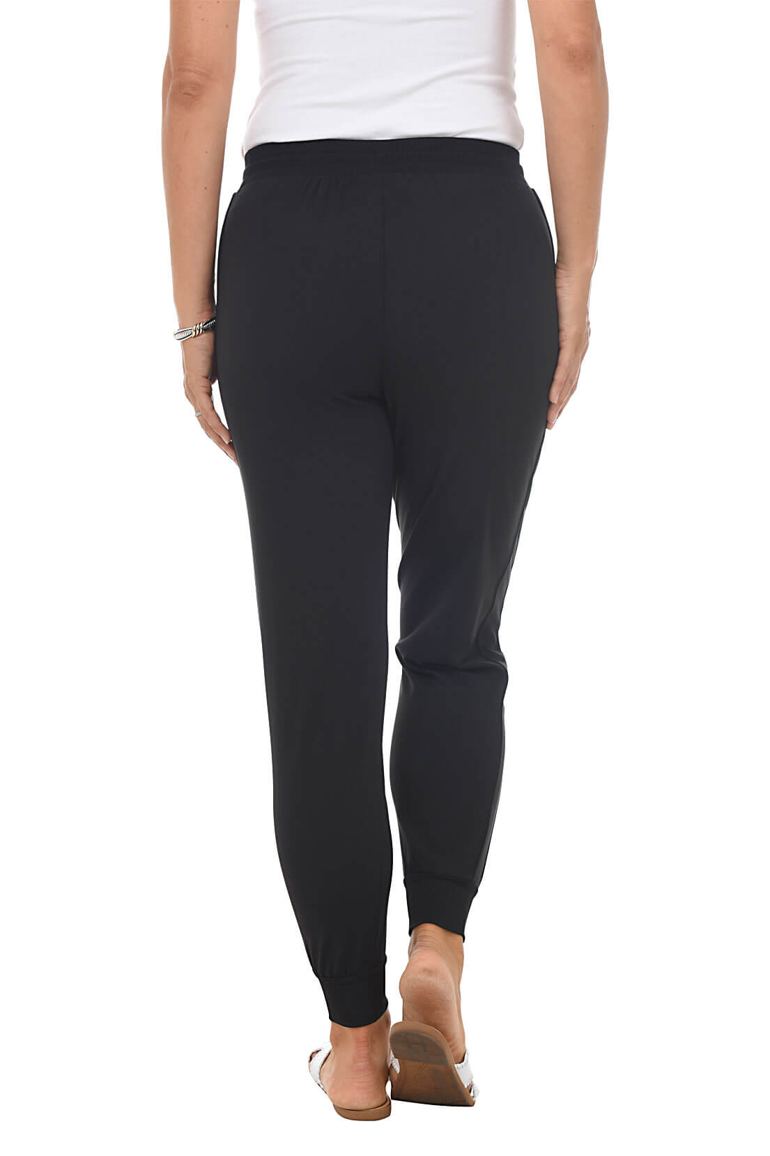 Person wearing black joggers and white top on a white background. Back shot.