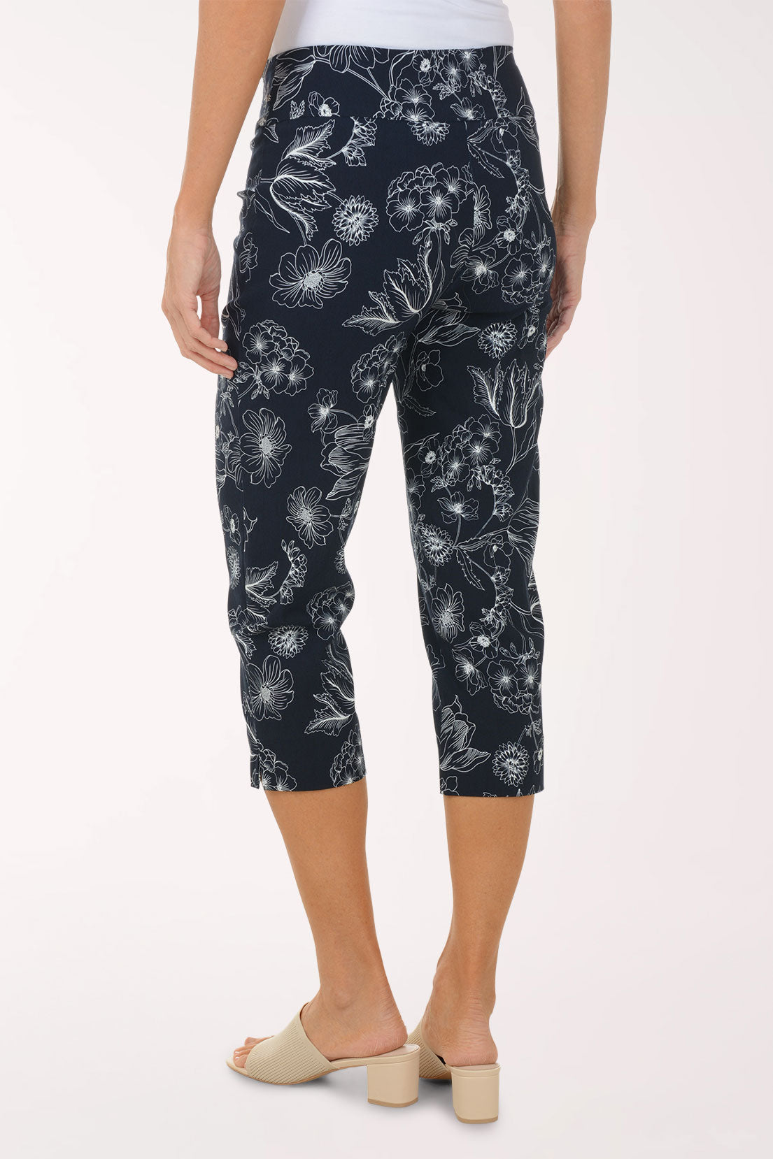 Person wearing navy capri pants with white floral pattern on a white background