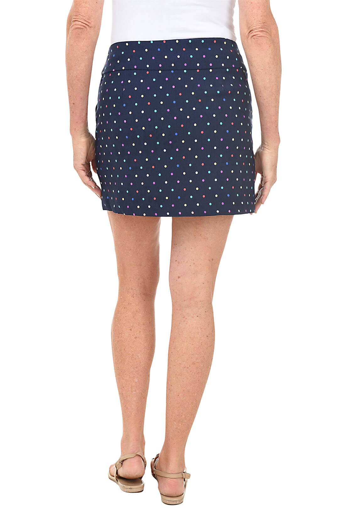 A back shot of a model navy skort with multicolor dots, with a elasticized waistband, knee-length, standing against a white background.