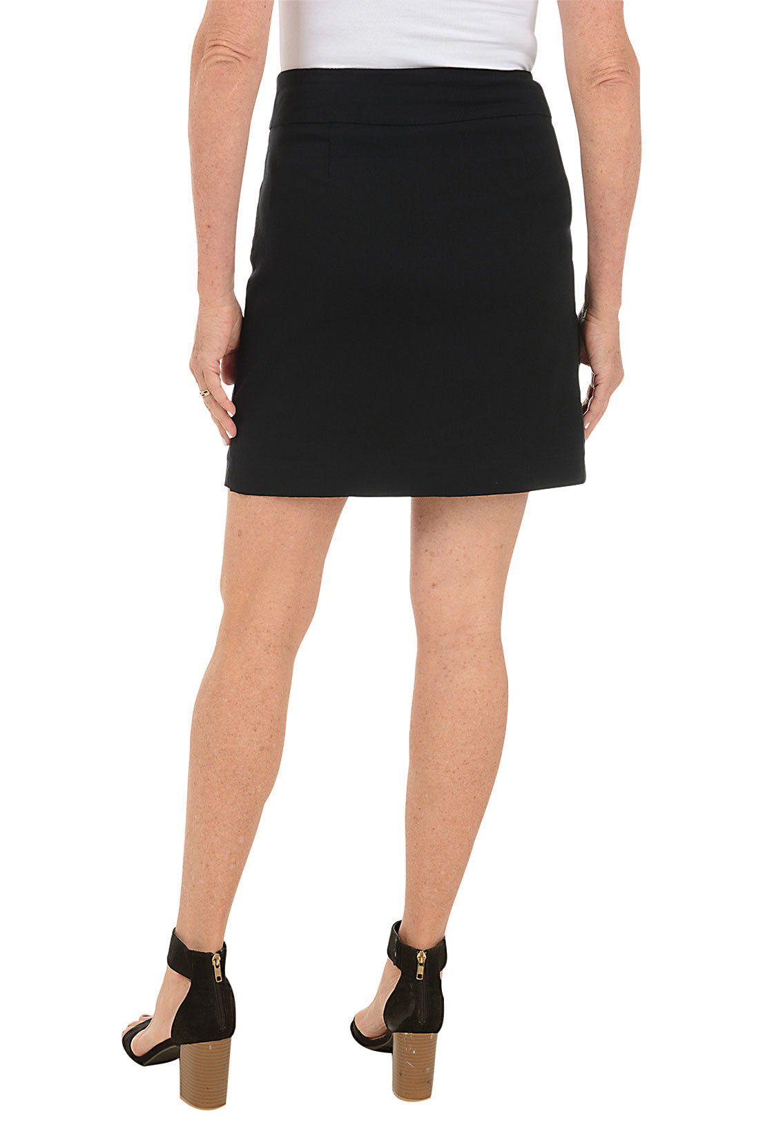 A back shot of a model wearing a black pull-on skort with dual front pockets, a straight hemline with side slits, paired with a white top and black heels.