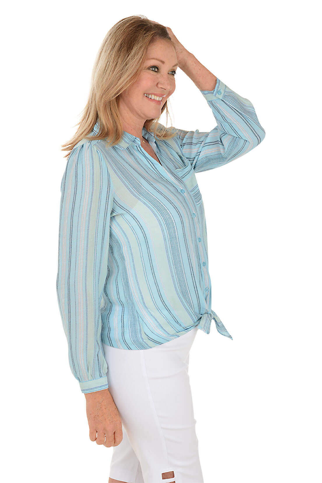 A side shot of a model wearing a blue striped long sleeve shirt with a classic foldover collar, buttoned cuffs, and a left chest pocket. The shirt is tied at the front, featuring a center back pleat and a curved hemline.