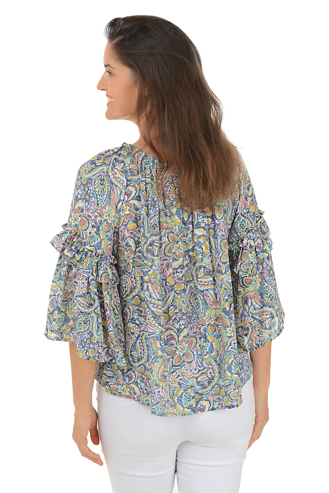 A back shot of a model wearing a floral paisley ruffled bell sleeve blouse with a scoop neck, in a multi-colored pattern. She is also wearing white pants.