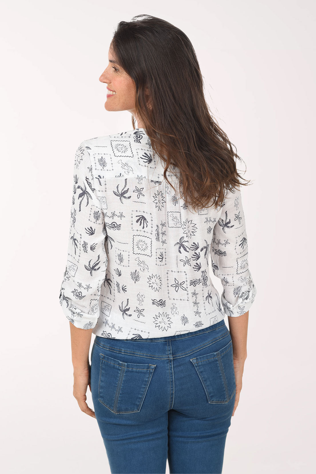 Woman wearing a white blouse with black patterns and blue jeans on a white background