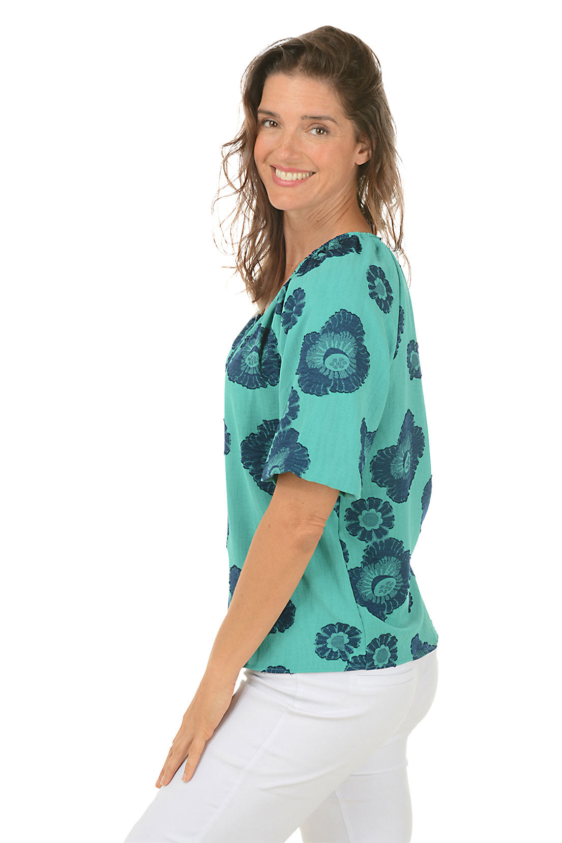 A side shot of a woman wearing a green and blue floral jacquard blouse with puffed sleeves and a V-neck.
