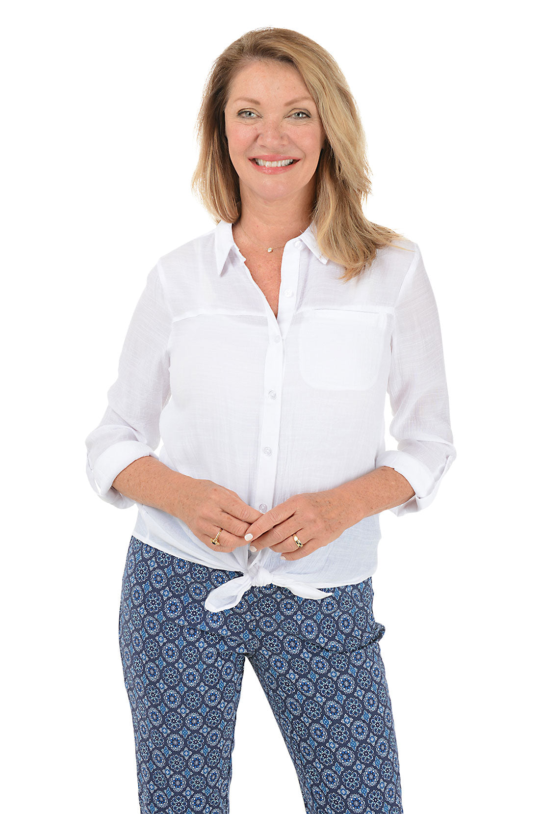 A front shot of a model wearing a white button-front shirt with a foldover collar, long sleeves, buttoned cuffs, and a left chest pocket. The shirt is tied at the front, creating a curved hemline.