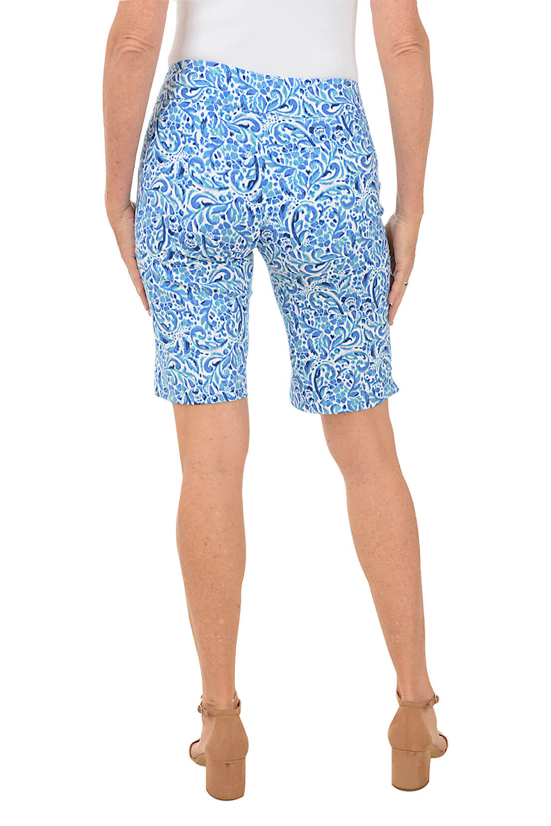 A back shot of a model wearing blue floral nebula pull-on bermuda shorts with a white top, standing against a white background.