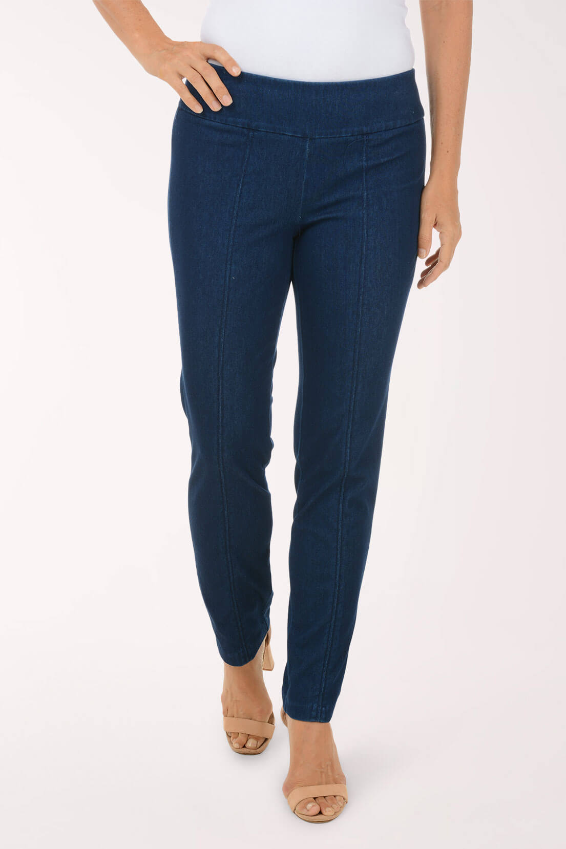 A front view of dark wash slim leg pull-on jeans with a smooth waistband and center leg seams, worn with nude heels.