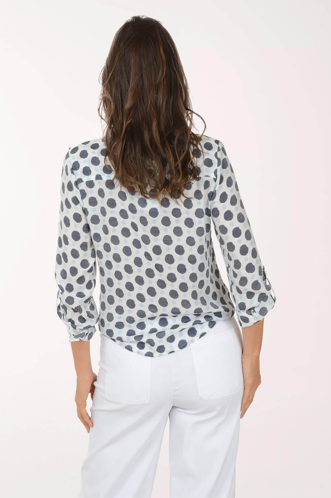 Woman wearing a polka dot blouse and white pants on a light pink background