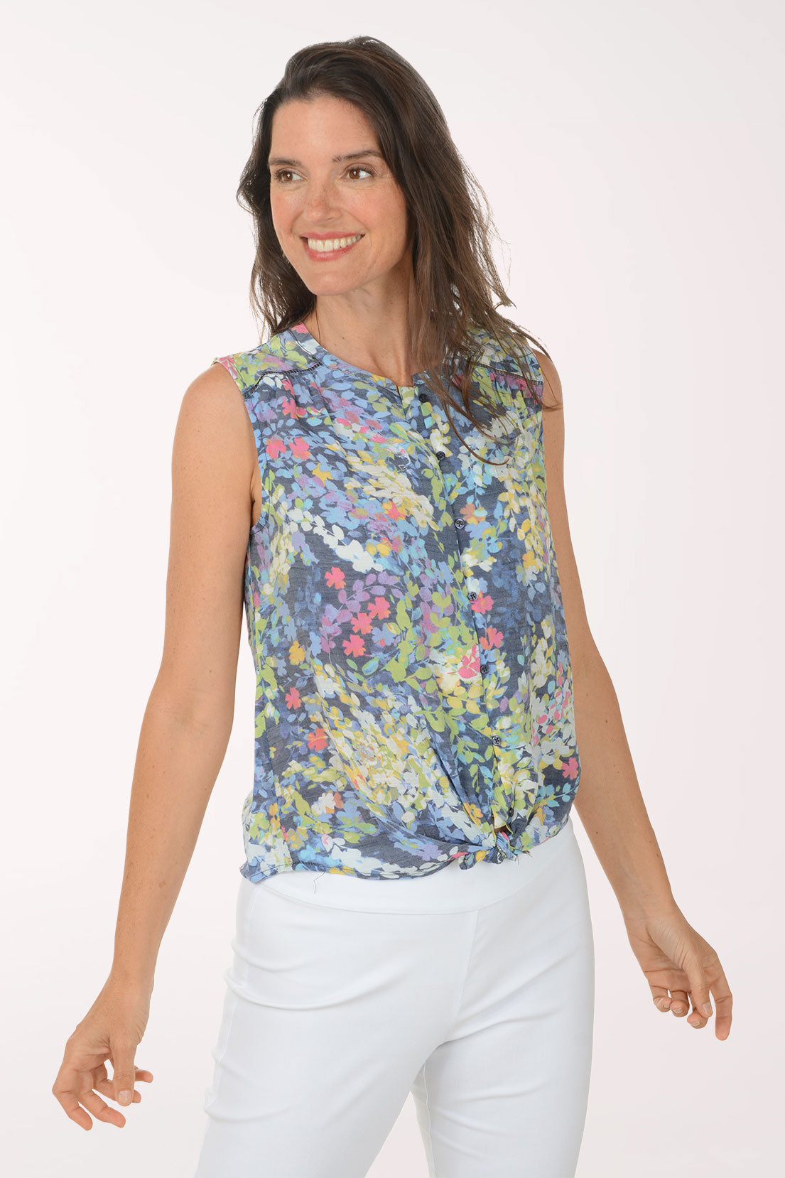 Woman wearing a sleeveless floral top and white pants on a white background