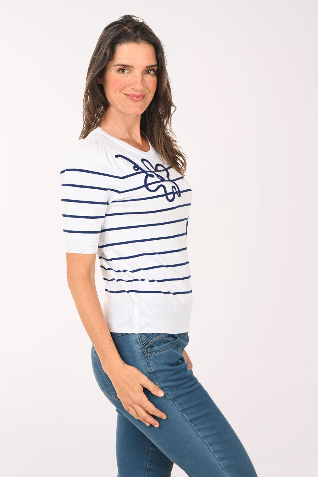 Woman wearing a white and blue striped sweater with a floral logo, standing against a plain background