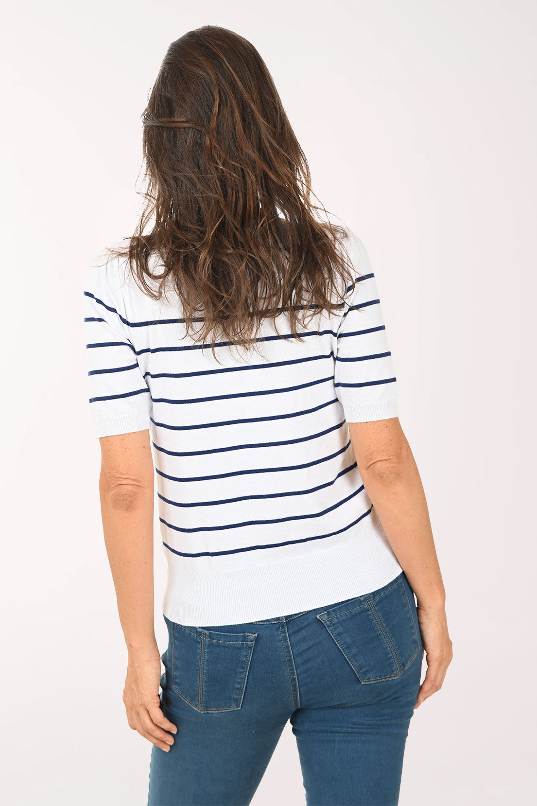 Woman wearing a white and blue striped sweater with a floral logo, standing against a plain background