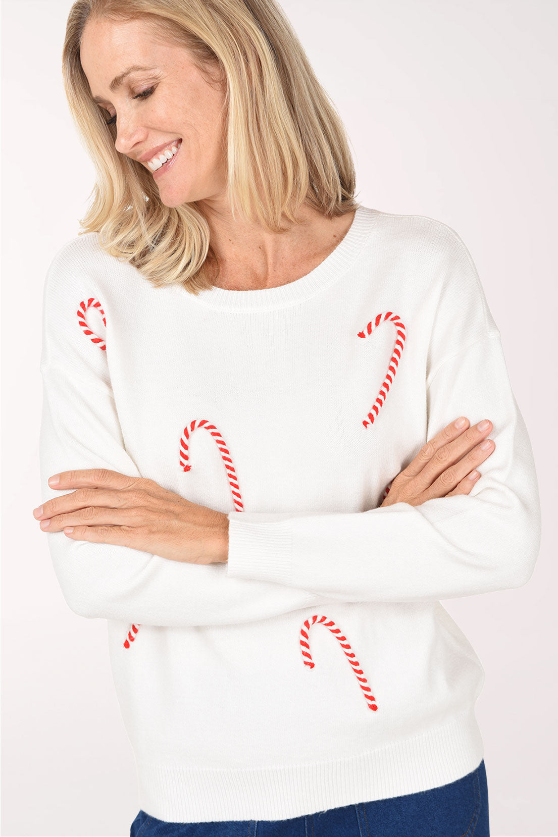 Model with arms crossed in the ivory Candy Cane Sweater, showing the twisted red and white candy cane details and ribbed cuffs