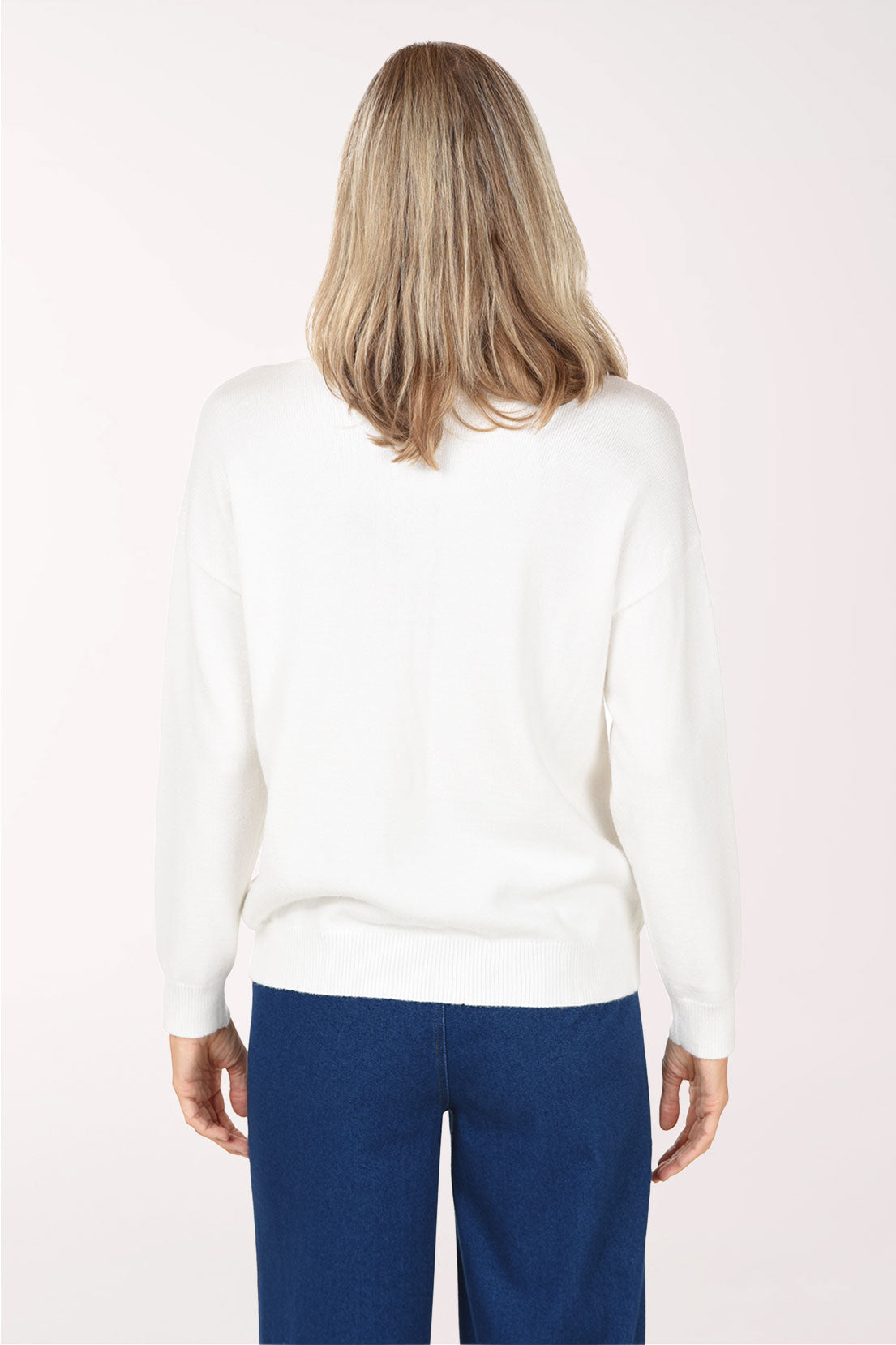 Back view of the Candy Cane Sweater in plain ivory knit with a ribbed hem, worn with dark blue jeans
