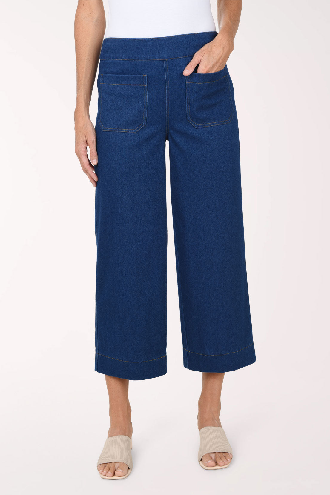 A front view of medium wash wide leg cropped pull-on jeans with a smooth waistband and front patch pockets, worn with nude slide sandals.
