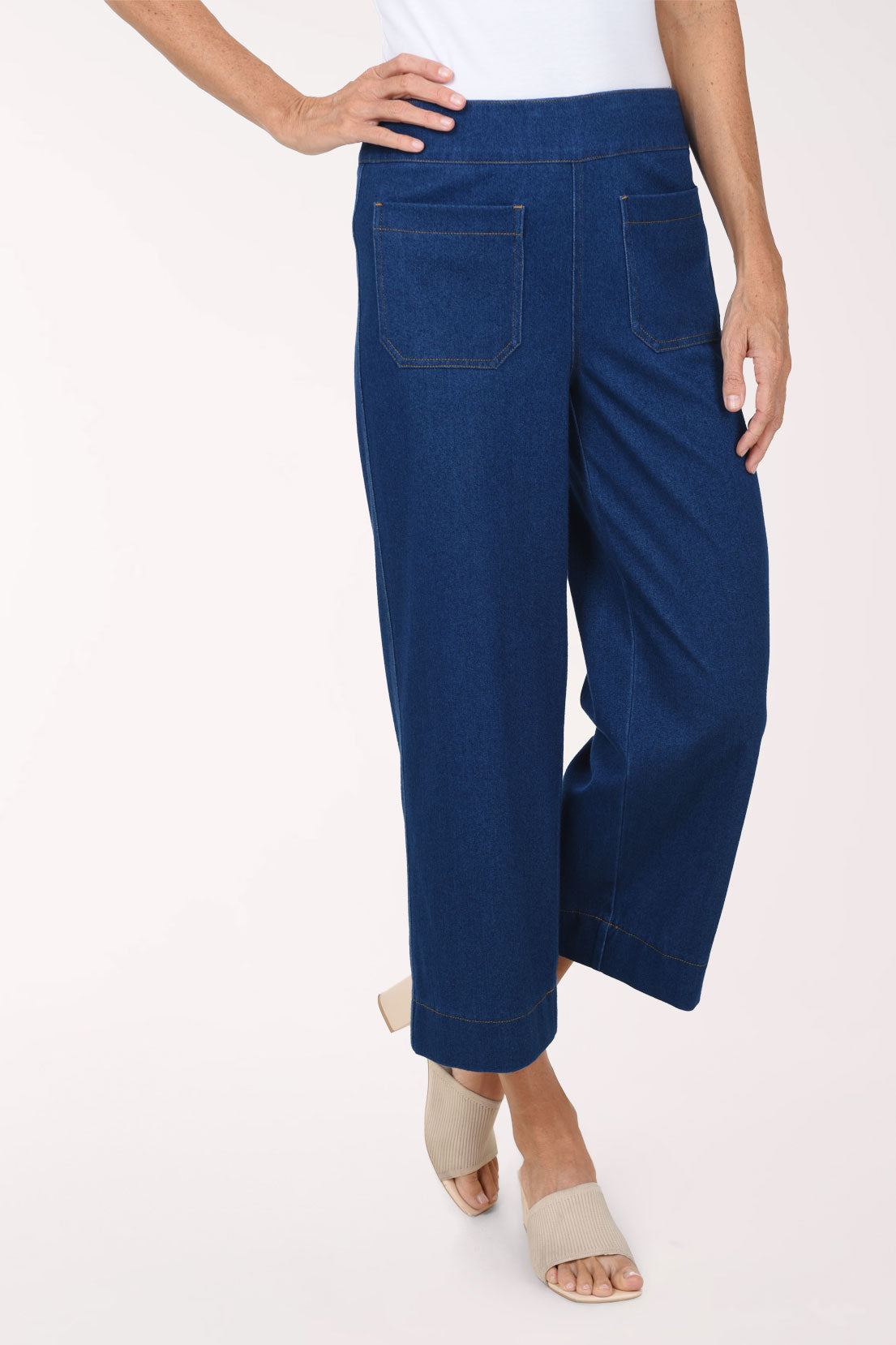 A front view of medium wash wide leg cropped pull-on jeans with one hand on the hip.