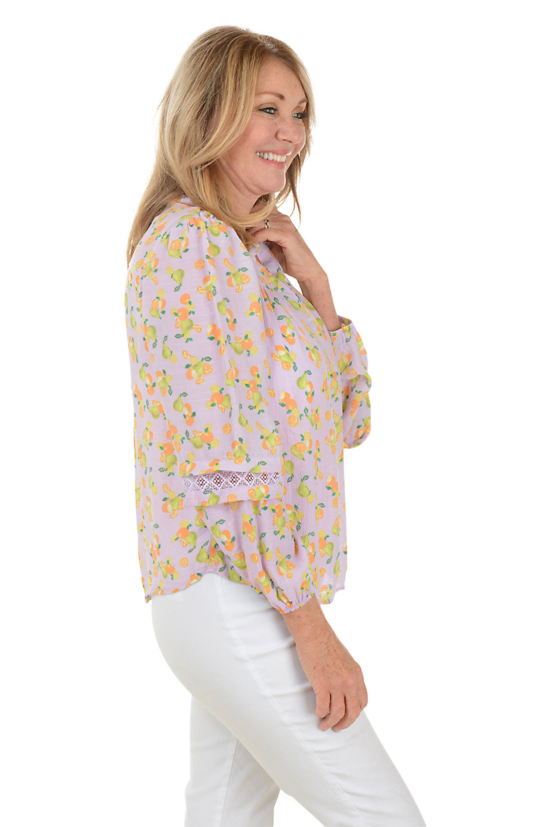 A side shot of a woman wearing a long puffed sleeve blouse with a floral pattern, featuring a split v-neckline with ruffled collar, pleated styling with crochet trim on shoulders and sleeves, and elastic cuffs.