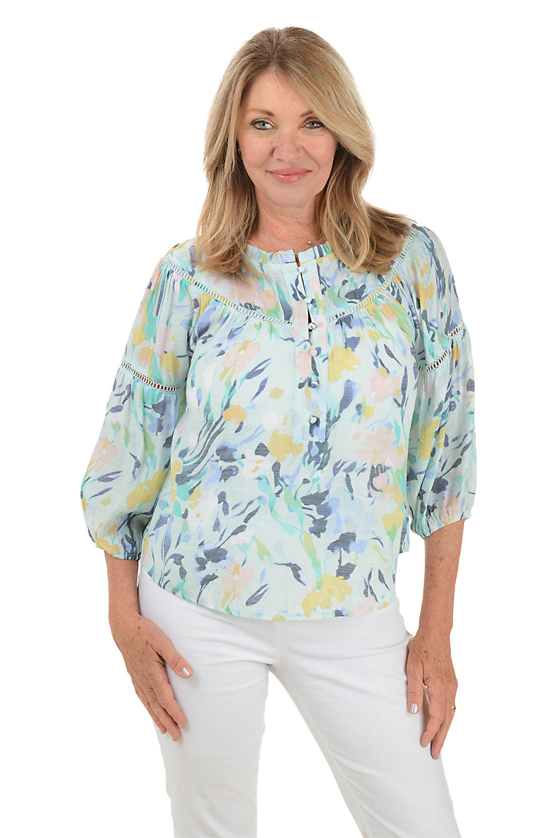 A front shot of a model wearing a floral print crochet puff sleeve blouse with a scoop neckline and buttoned half placket, paired with white pants.