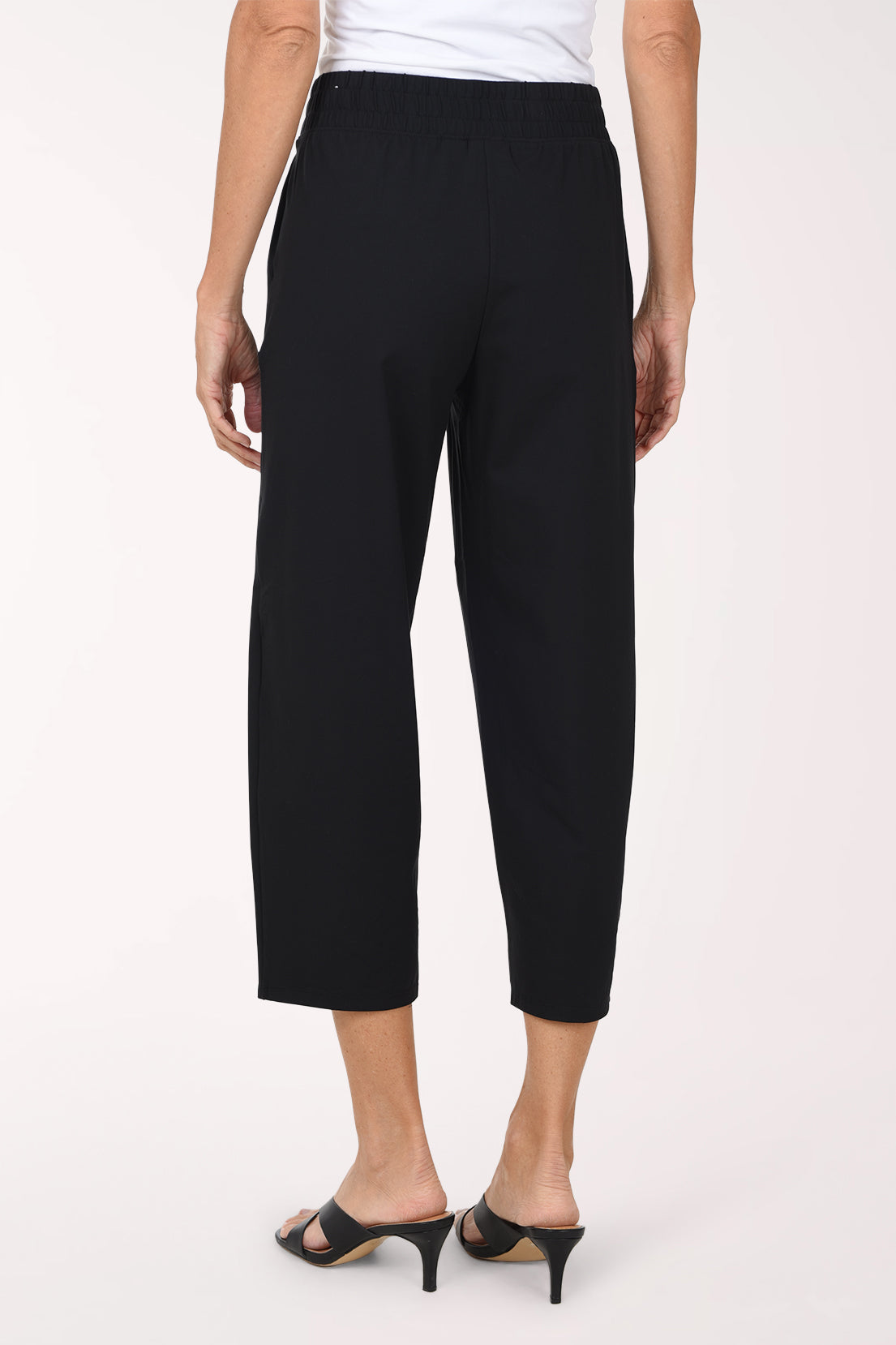 A model wearing black cropped activewear pant, paired with a white top and black sandals, against a plain light background.