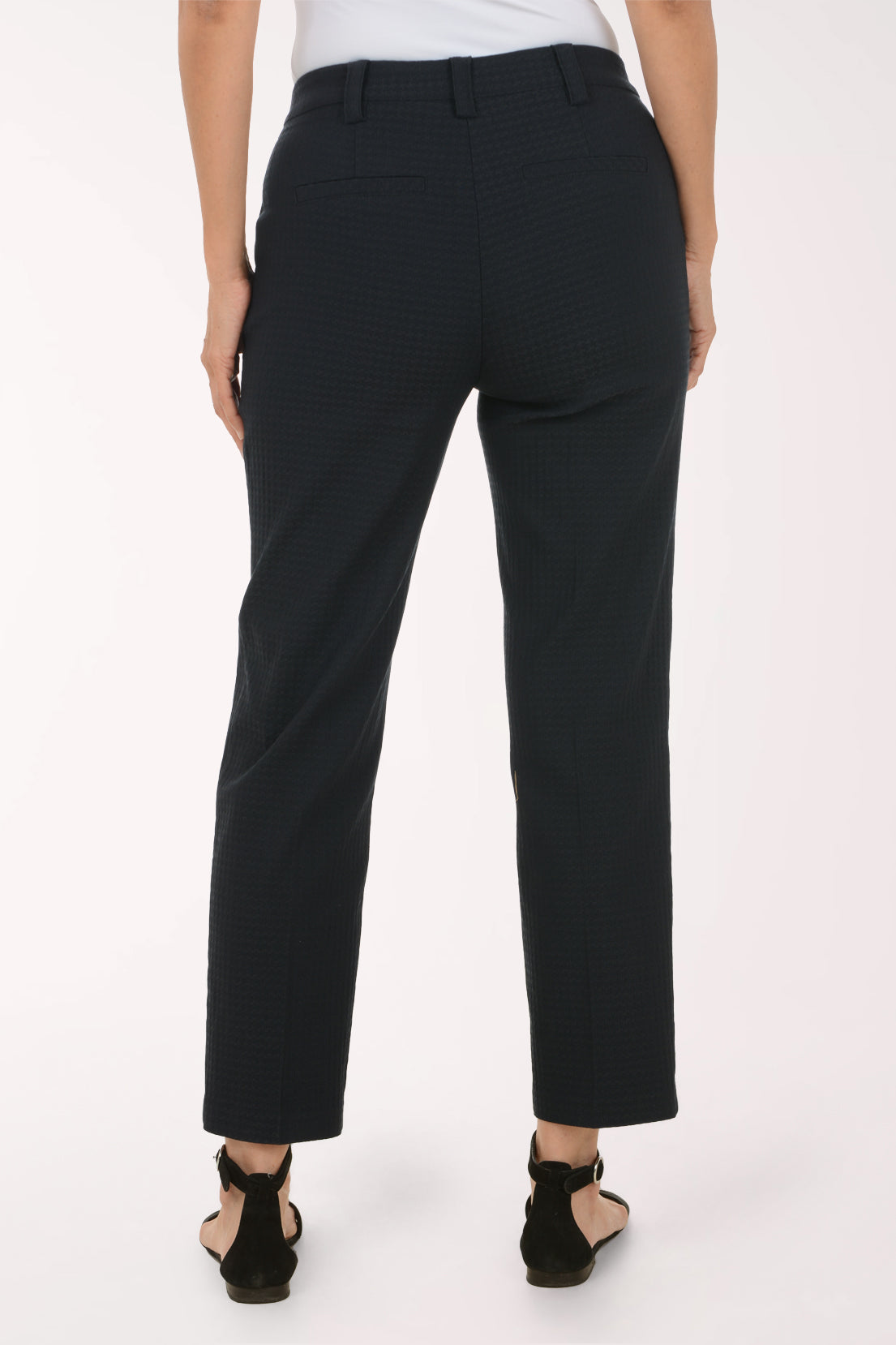 A person shown from the back wearing dark charcoal cropped trousers with a subtle textured pattern, paired with black strappy sandals against a plain white studio background.