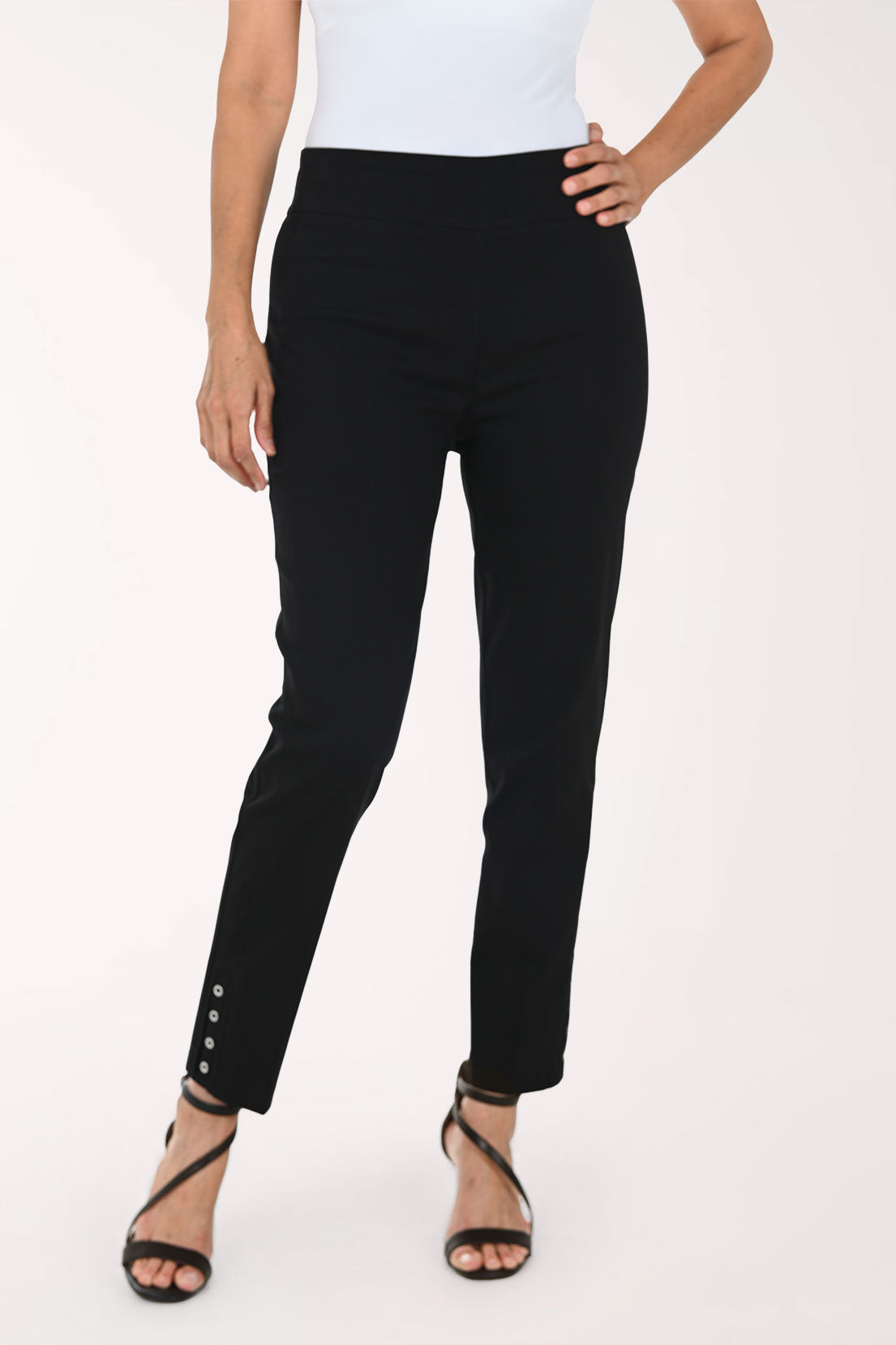 A model wearing black slim-fit ankle-length pants with decorative silver buttons on the lower hem, paired with a white top and black strappy heels, against a plain white studio background.