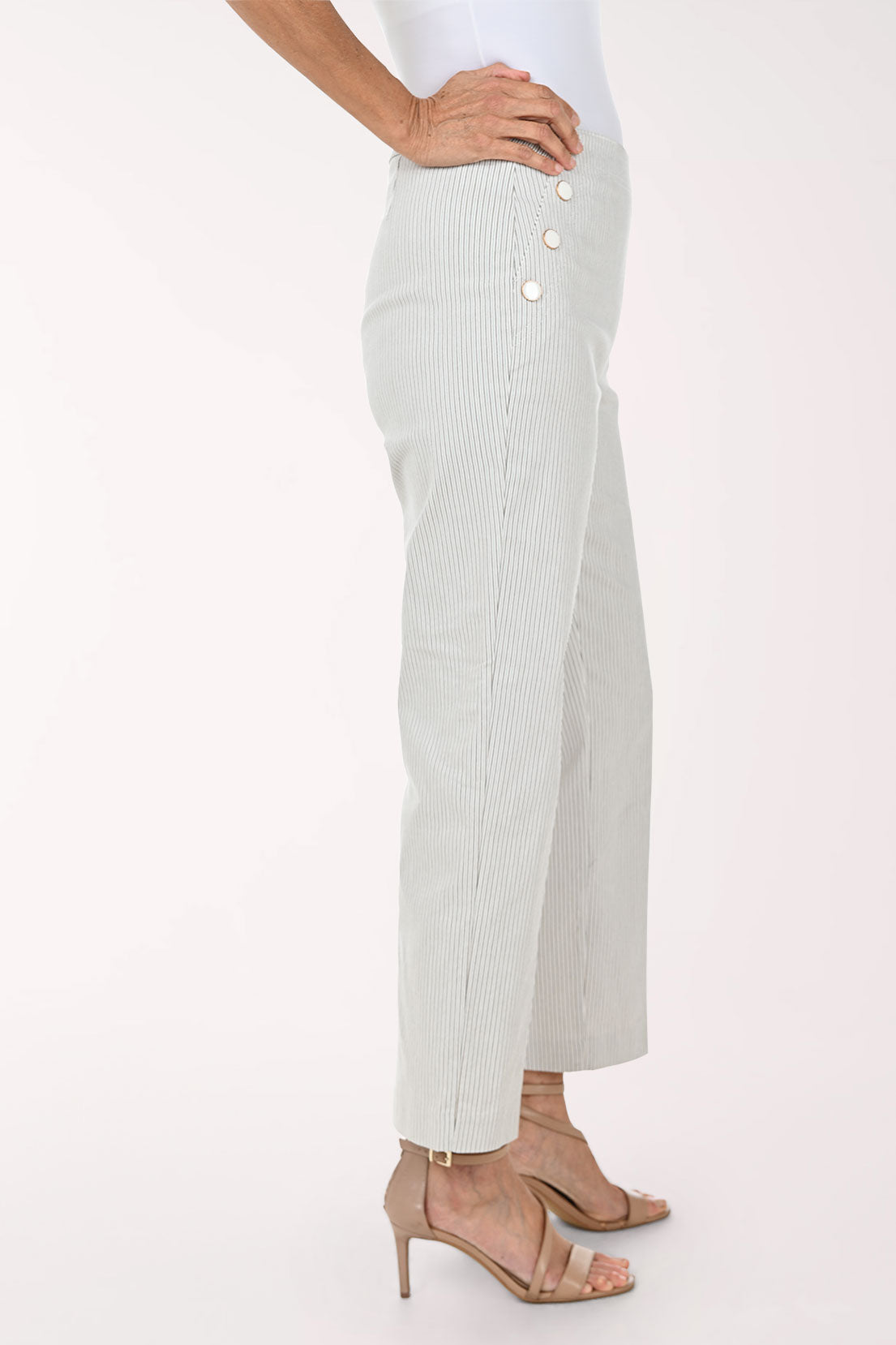 A model wearing light sage green pinstriped trousers with decorative gold buttons on the sides, paired with beige strappy high-heeled sandals against a plain white background.