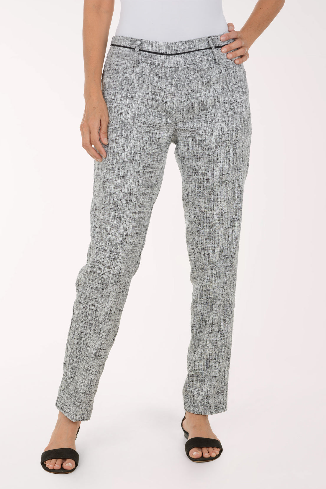 A model wearing a pair of slim-fit trousers in a gray and white textured tweed pattern, paired with black slide sandals against a plain white studio background.