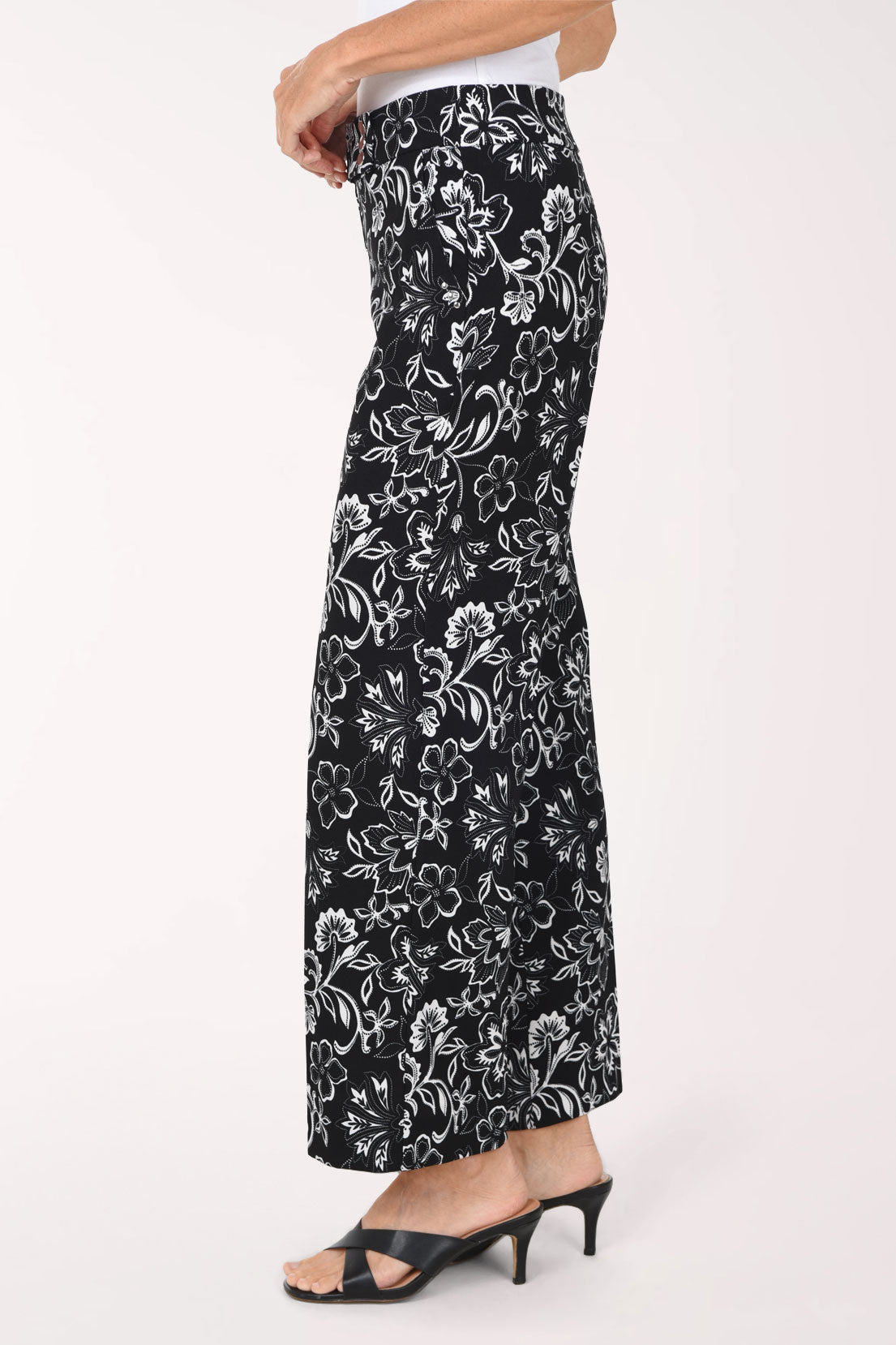 A person wearing black wide-leg cropped pants with a white floral print, paired with a white top and black slide sandals, shown against a plain light background.