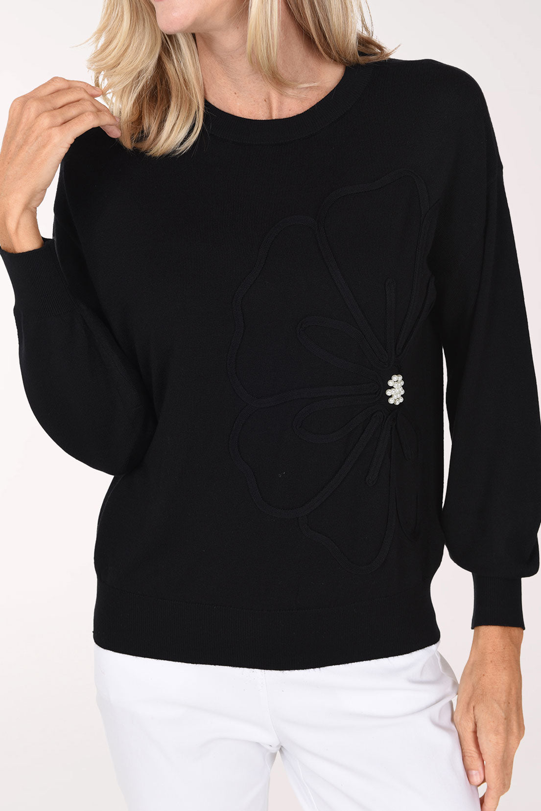 Woman wearing a sold black sweater with a pearl button accent on waist
