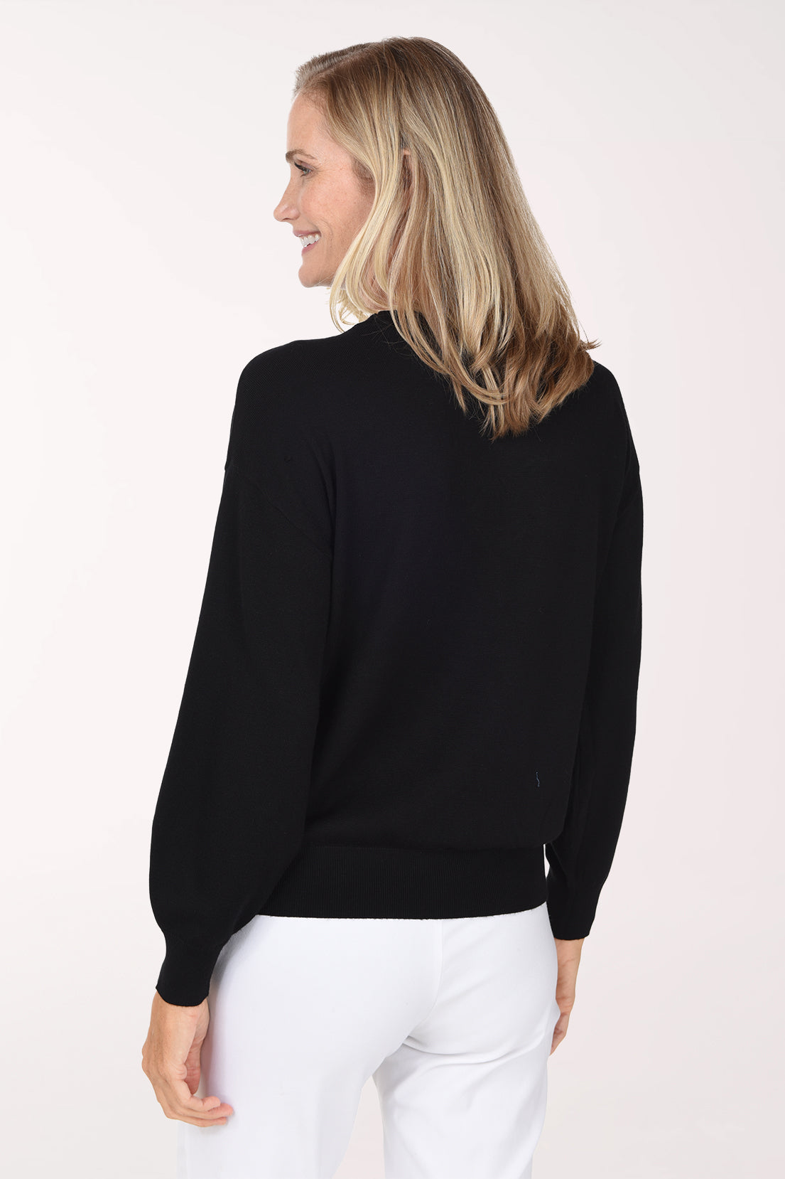 Woman wearing a sold black sweater with a pearl button accent on waist