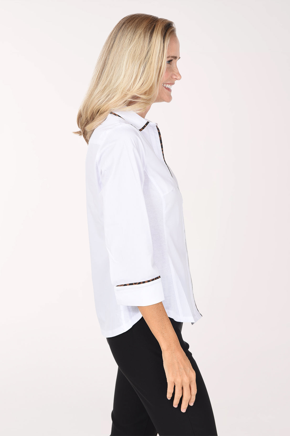 A woman shown in side profile wearing a white button-up shirt with animal print trim along the collar, placket, and rolled cuffs, paired with black pants, against a plain light background.