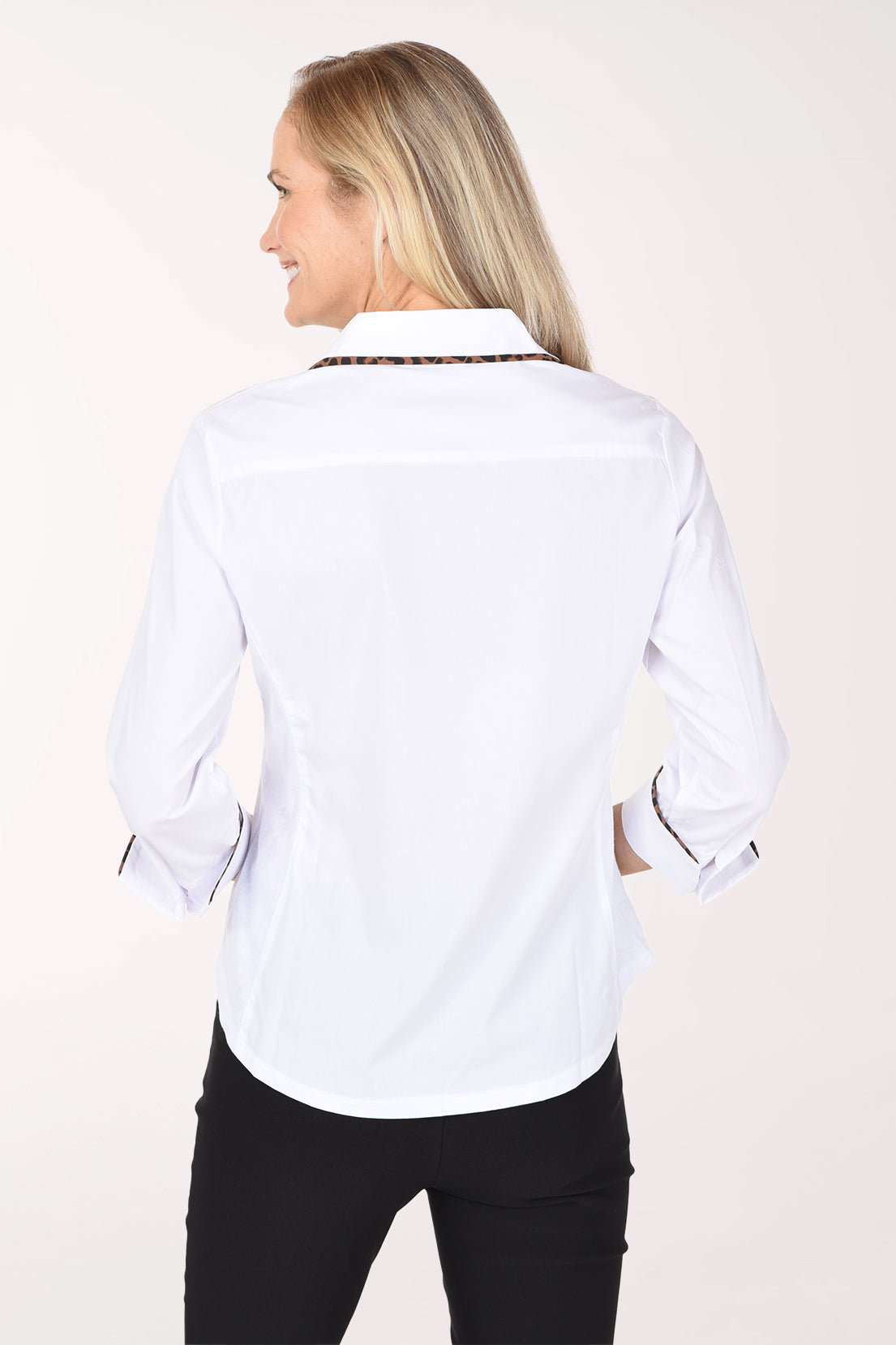 A woman wearing a white button-up shirt with animal print trim along the collar, placket, and rolled cuffs, paired with black pants, against a plain light background.